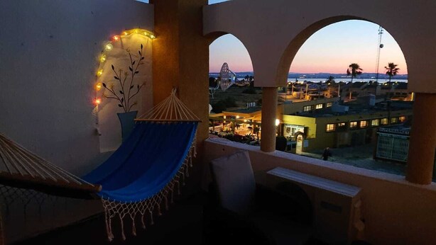 A balcony with a hammock, a potted plant, and a view of a cityscape at dusk. - House with roof terrace (Torrevieja)