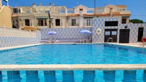 A swimming pool with clear blue water, checkered walls, and a few umbrellas. - House with roof terrace (Torrevieja)