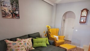 A living room with a dark grey sofa, green and patterned pillows, a small round table with a white candle, a yellow armchair, and a painting on the wall. - House with roof terrace (Torrevieja)