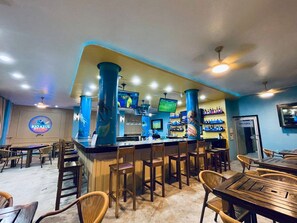A bar area with wooden tables and chairs, a counter with a TV screen, and a sign reading 'RIO AZUL BAR & GRILL'. - Hotel Royal Blue & Golf Cart Rental (San Pedro)