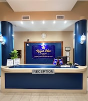 Een receptiebalie bij het Royal Blue Hotel met een bord waarop in- en uitchecktijden staan, een telefoon en een plant.