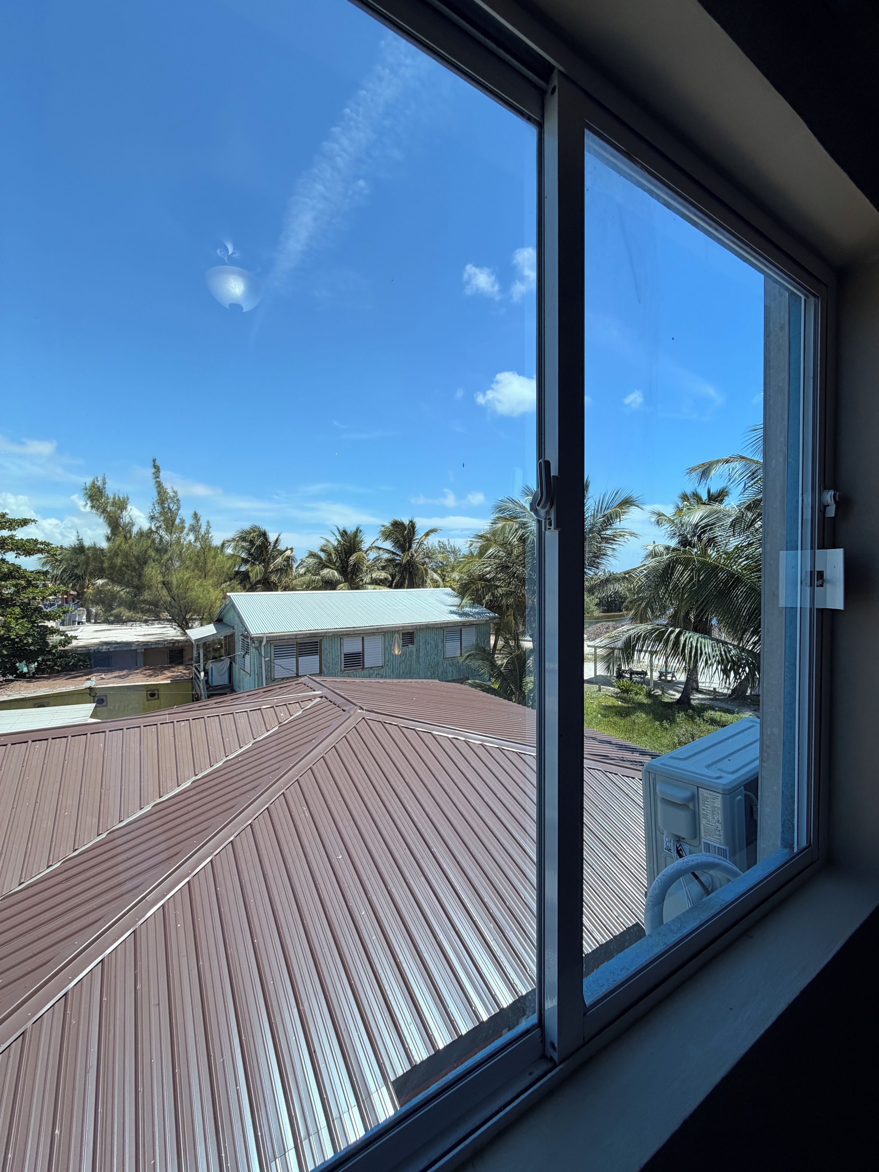 Vista desde una ventana con un muelle de madera y cielo azul.