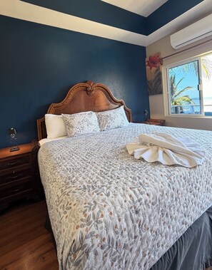 A bedroom with a large bed, wooden headboard, and a window with a view of palm trees. - Hotel Royal Blue & Golf Cart Rental (San Pedro)