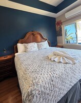Een slaapkamer met een groot bed, houten hoofdeinde en een raam met uitzicht op palmbomen.