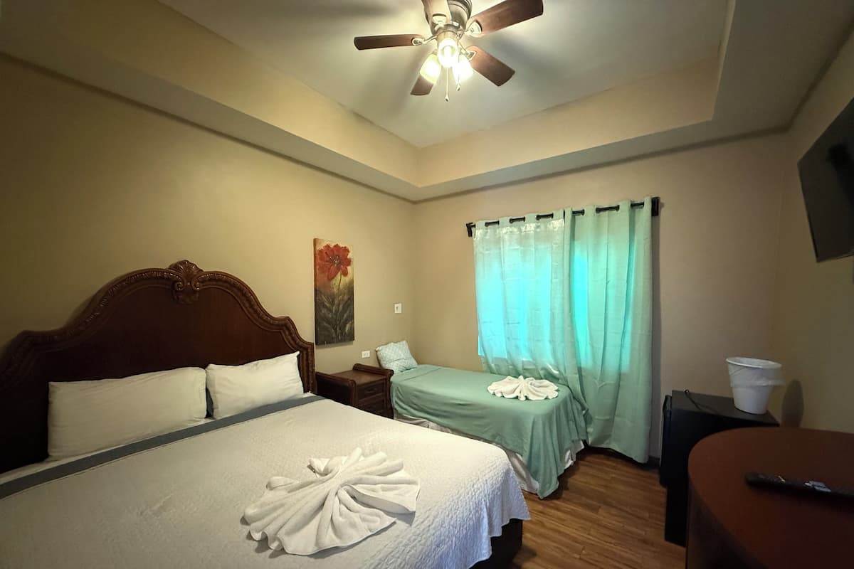 A hotel room with a bed, a nightstand, a desk, a ceiling fan, and a window with curtains.