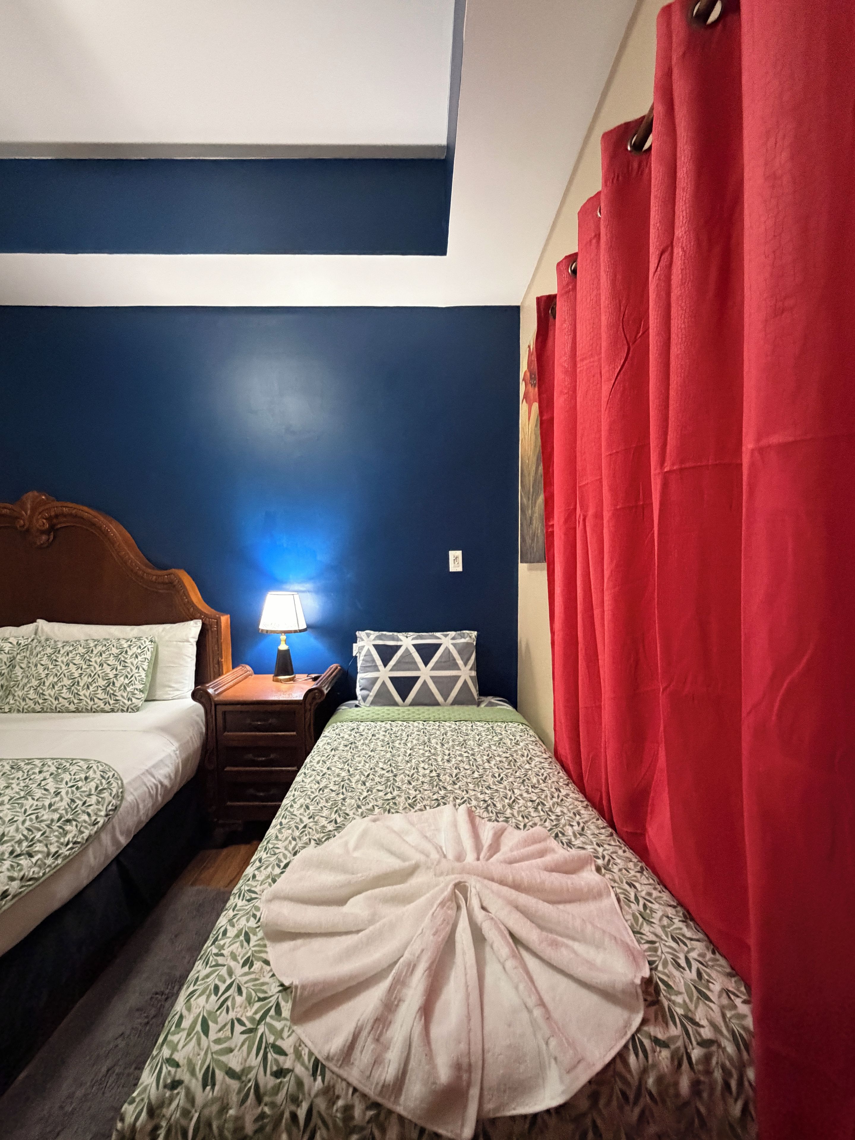 Un dormitorio con dos camas, una mesita de noche con lámpara y una cortina roja.