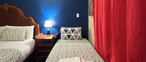 Une chambre avec deux lits, une table de chevet avec une lampe et un rideau rouge.