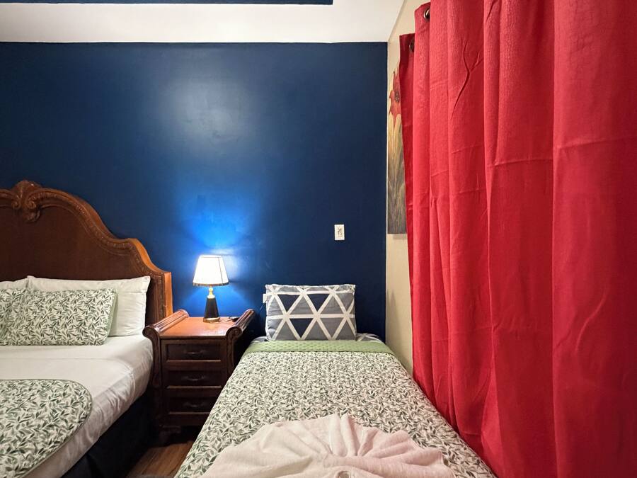 Un dormitorio con dos camas, una mesita de noche con lámpara y una cortina roja.