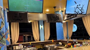 A bar area with two TVs displaying sports, a counter with various items, and a view of the outside.
