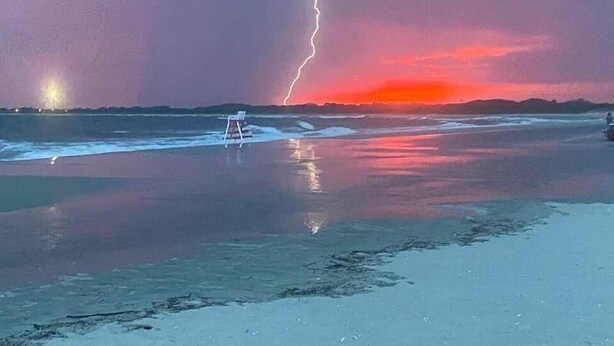 Ranta, jossa on pelastustorni, ja taivaalla näkyy salamanisku.