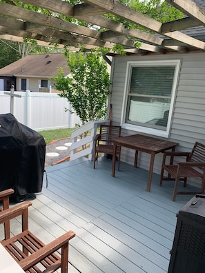 Relax on the covered patio with a table and chairs under a pergola, adjacent to a charming house with a white picket fence.