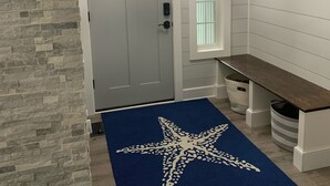 Käytävä, jossa on kiviseinä, sininen meritähtikuvioinen matto, valkoinen ovi ja penkki.