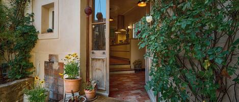 A rustic entrance with a wooden door, potted plants, and a brick pathway leading to a tiled interior.