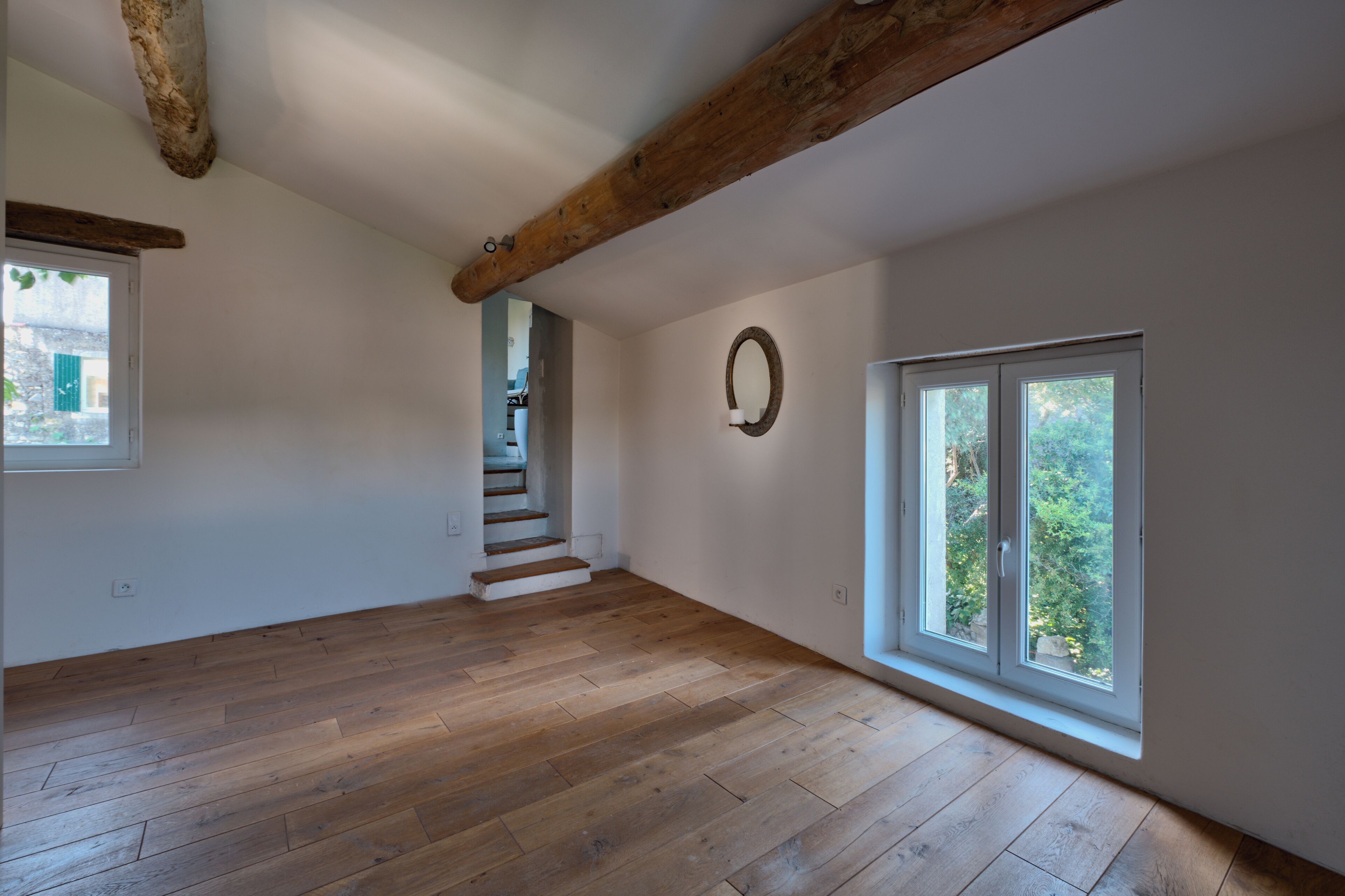 Una habitación amplia con piso de madera, una escalera y ventanas grandes.