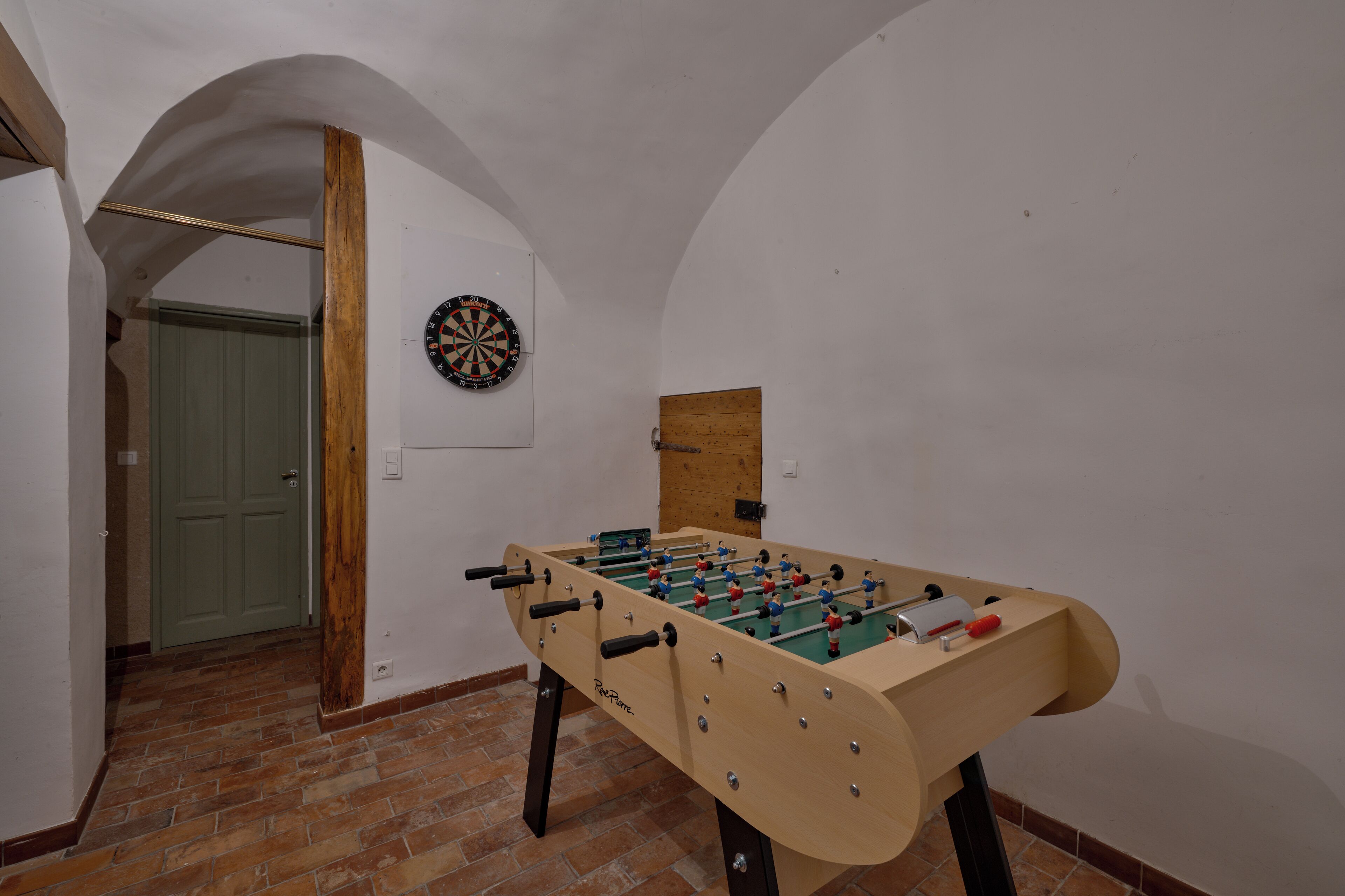 A foosball table in a room with a dartboard and a wooden door.