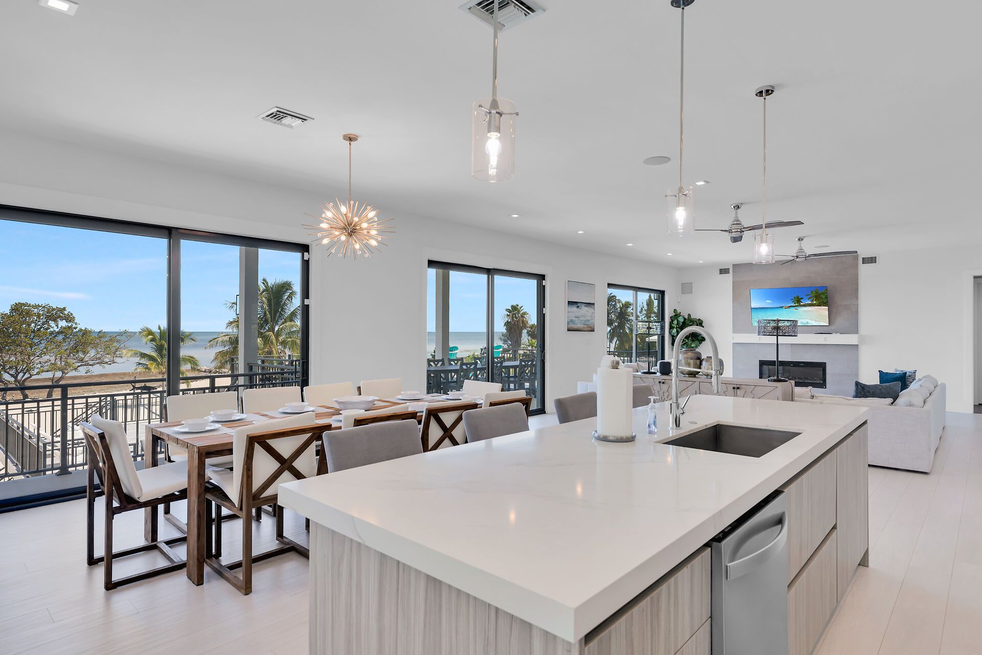 A modern kitchen with a large island, dining area with chairs, and a view of the beach.