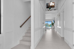 A modern interior with a staircase leading to a second floor, a hallway with a view to the outside, and a ceiling with recessed lighting.