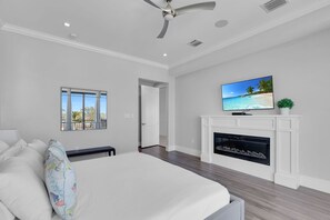 Une chambre avec un grand lit, un ventilateur de plafond, une cheminée et un téléviseur fixé au mur.
