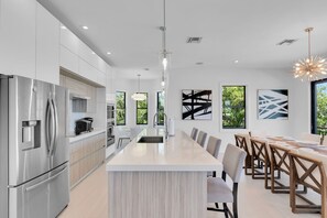 A modern kitchen with a central island, stainless steel appliances, and a dining area with wooden chairs. - Oceanfront 5BR | Pool, Beach & Atlantic Views (Marathon)
