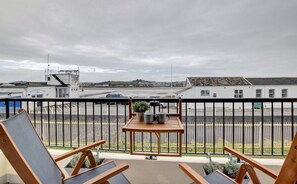 Uma varanda com vista para uma marina, uma mesa com um vaso de planta e duas cadeiras de descanso.
