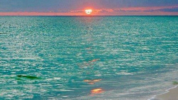 Una playa con un atardecer sobre el océano.