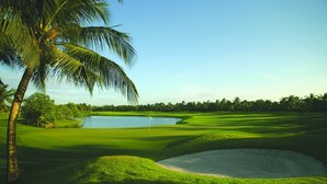 Campo de golf con obstáculo acuático, bunkers de arena y un mástil con bandera.