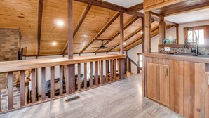 Un vaste espace de vie de style loft, avec des poutres apparentes, une cheminée en pierre et une vue sur l’étage supérieur.