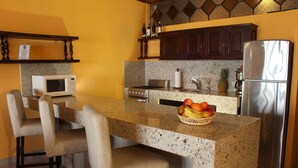 Una cocina con encimera de granito, microondas, estufa, refrigerador y una cesta de frutas.