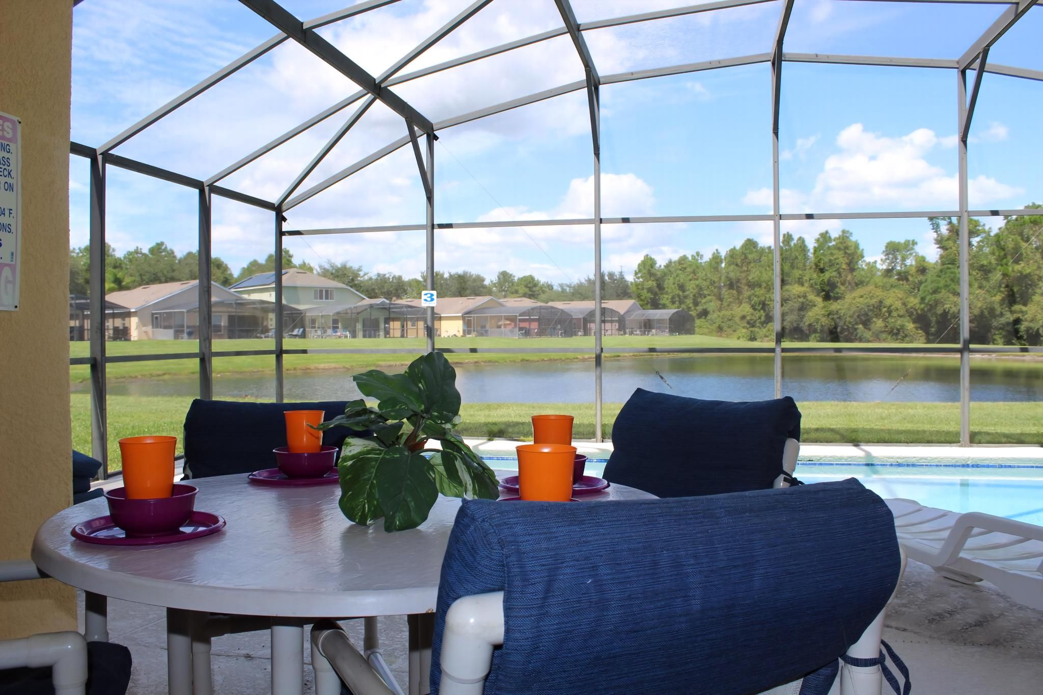 Un espace extérieur abrité, aménagé pour les repas, avec une table, des chaises et une vue sur un lac et des maisons.