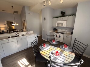 A compact kitchen with white cabinets, a microwave, and a stove. There is a dining table with chairs and red cups.