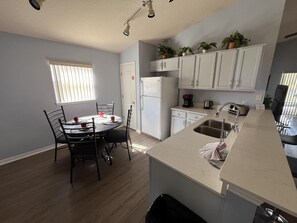 A compact kitchen with a dining area, white cabinets, a refrigerator, and a coffee maker.