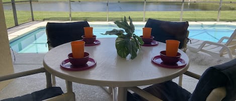 A round table with four orange cups and a green plant in the center, surrounded by four chairs with dark cushions.