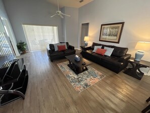A modern living room with two black leather sofas, a coffee table, and a ceiling fan.