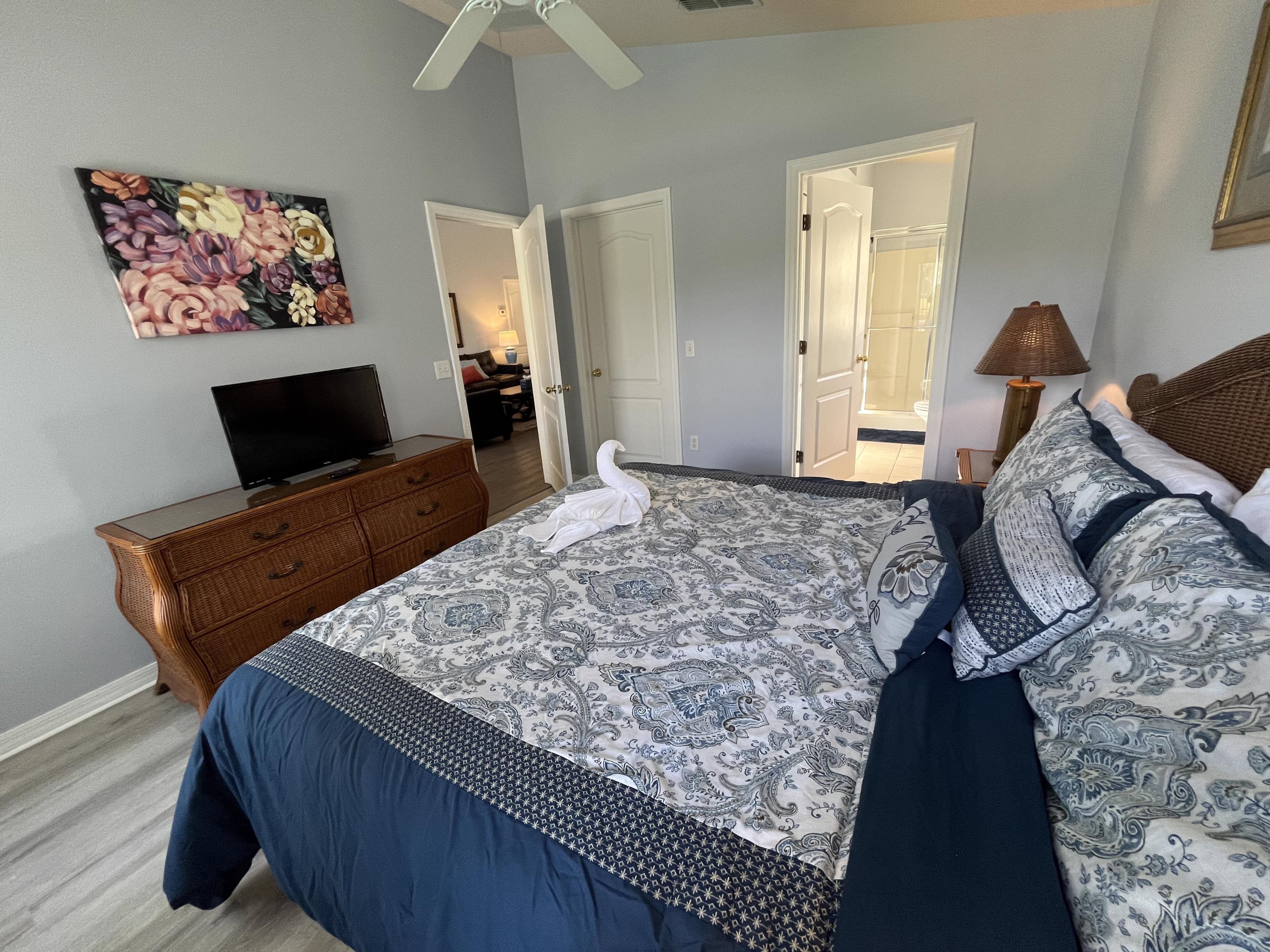Une chambre à coucher avec un lit, une commode, un téléviseur et un tableau accroché au mur.