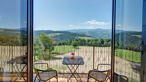 A balcony with a table and two chairs, overlooking a scenic landscape with hills and trees.