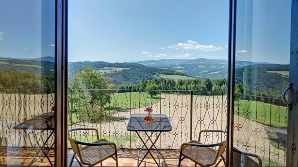 A balcony with a table and two chairs, overlooking a scenic landscape with hills and trees.
