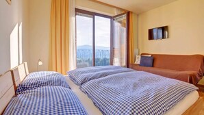 A hotel room with two beds, a sofa, a TV, and a balcony with a view.