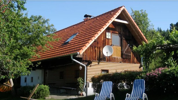 A wooden cabin with a sloped roof, a satellite dish, and a large window.