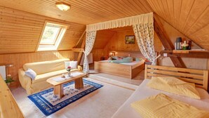 A cozy attic bedroom with a wooden ceiling, a bed with a canopy, a sofa, a small table with a vase, and a window with curtains.