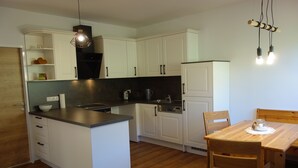A compact kitchen with white cabinets, a wooden dining table, and a hanging light fixture.