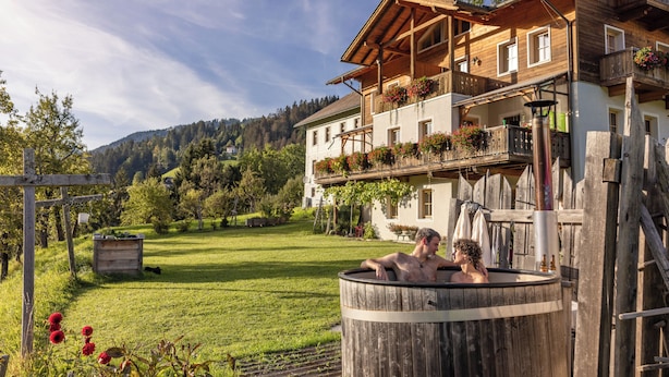 Un chalet de madera con jacuzzi, un balcón lleno de flores y vistas al bosque.
