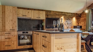 Una cocina con muebles de madera, horno empotrado, comedor con mesa y sillas, y un ventanal grande.