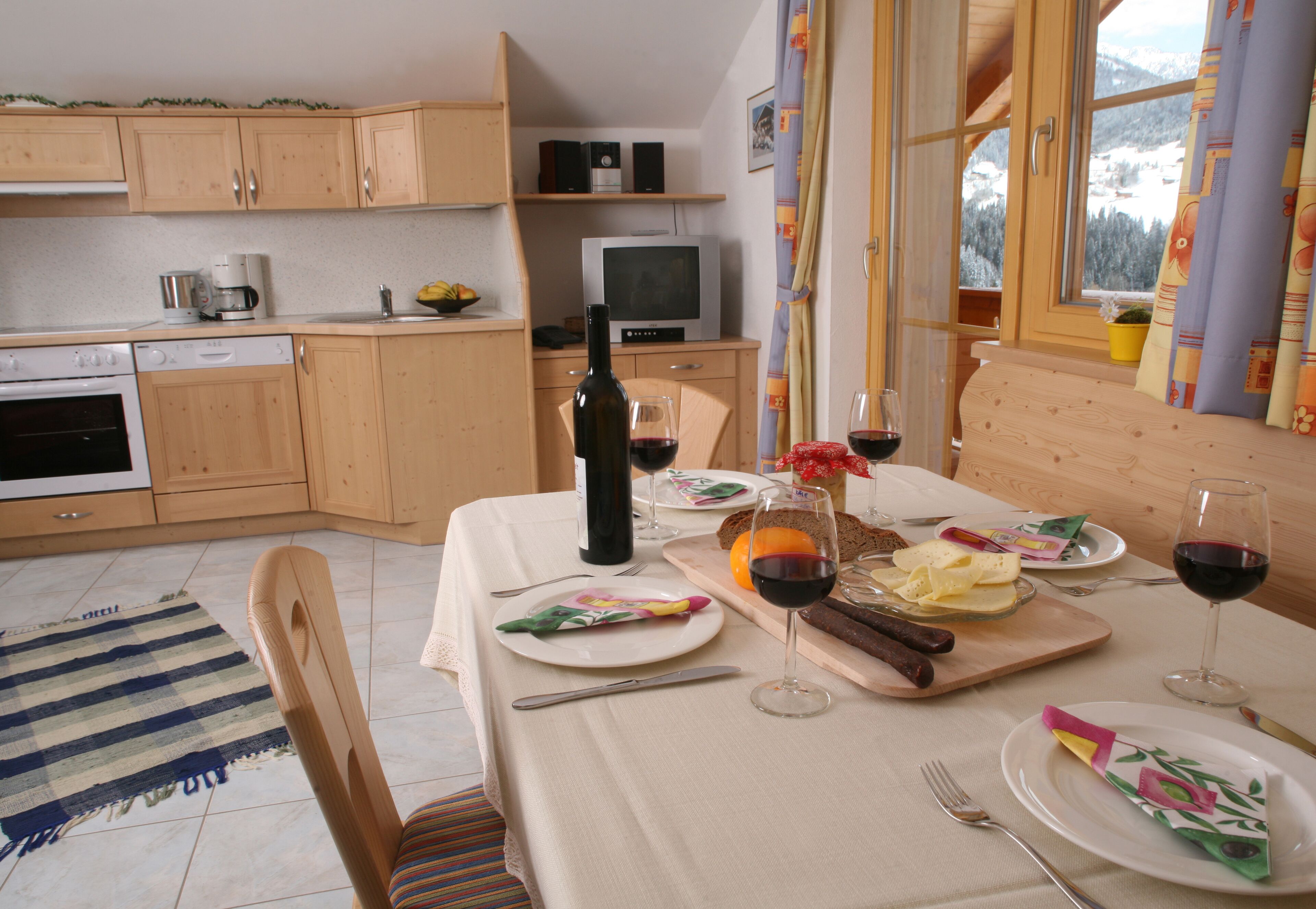 Un comedor con una mesa lista para dos personas, una botella de vino y un televisor al fondo.