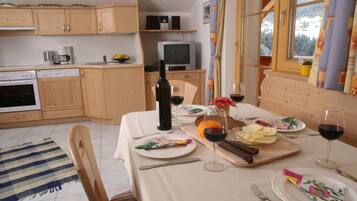 Un comedor con una mesa lista para dos personas, una botella de vino y un televisor al fondo.