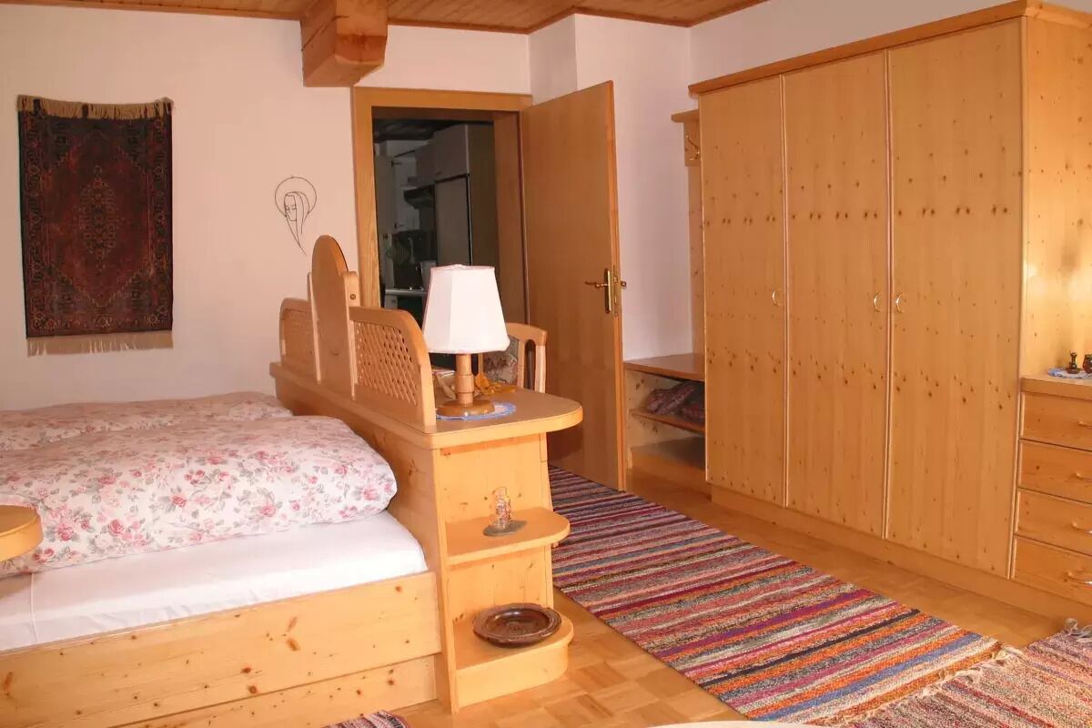 A bedroom with wooden furniture, a bed, a desk, a wardrobe, and a colorful striped rug.