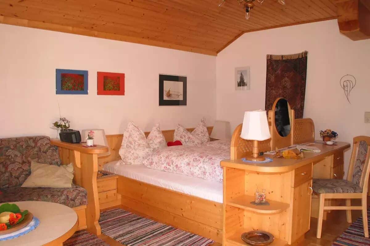 Una habitación acogedora con una cama, un escritorio de madera, una silla y una mesita con un cuenco de fruta.