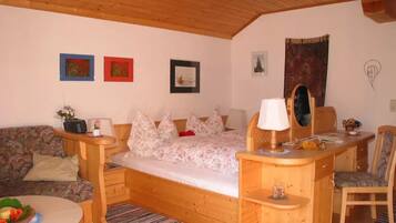 Ein gemütliches Zimmer mit einem Bett, einem Holztisch, einem Stuhl und einem kleinen Tisch mit Obstschale.