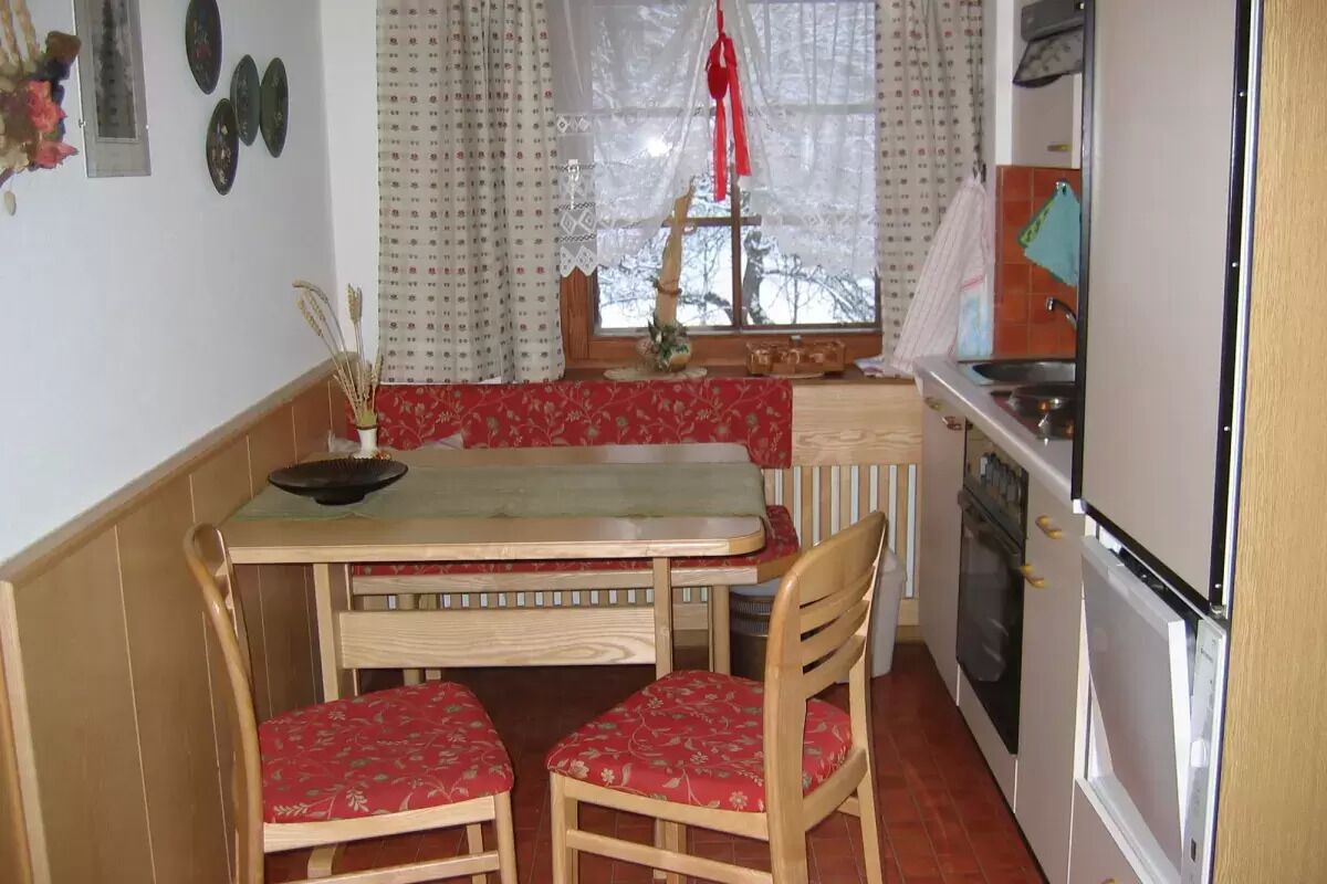 Une cuisine de taille réduite comprenant une table et des chaises, une fenêtre avec des rideaux et les appareils électroménagers de base.