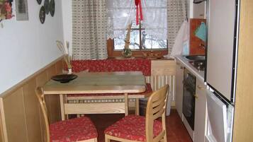 Une cuisine de taille réduite comprenant une table et des chaises, une fenêtre avec des rideaux et les appareils électroménagers de base.