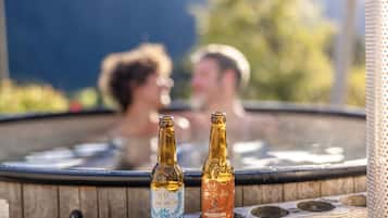 Una vasca idromassaggio con due bottiglie di birra, panche di legno e sullo sfondo figure sfocate.